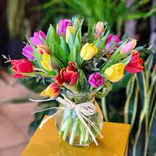 How to Remove Watermark from PicsArt Easily in 2025 2 Vivid tulip bouquet in a clear vase with string bow, set on yellow surface against leafy backdrop.